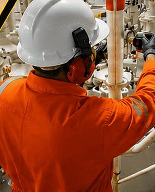 Técnico com capacete e protetor auricular em área industrial